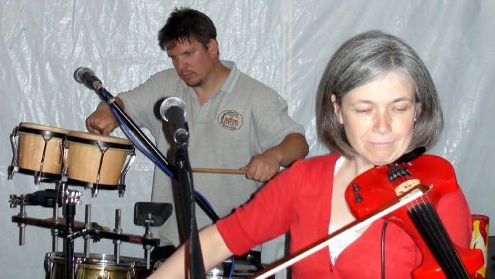 Eclectix fiddle player in red, mid-set, with the percussionist behind
